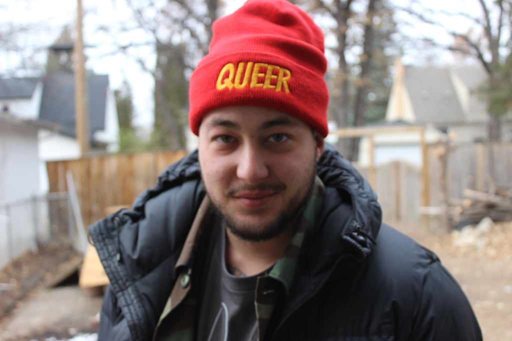 Red Toque with the word "Queer" embroidered in yellow thread. Model: Ro Walker Mills he/him