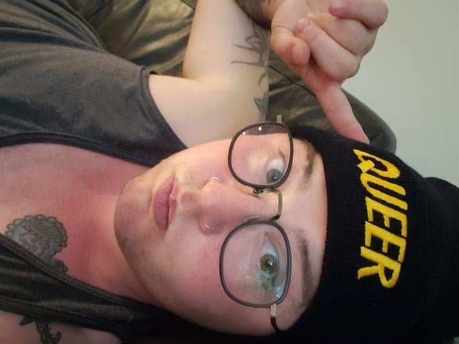 Black toque with the word Queer embroidered in yellow thread. Model: Elliott he/him